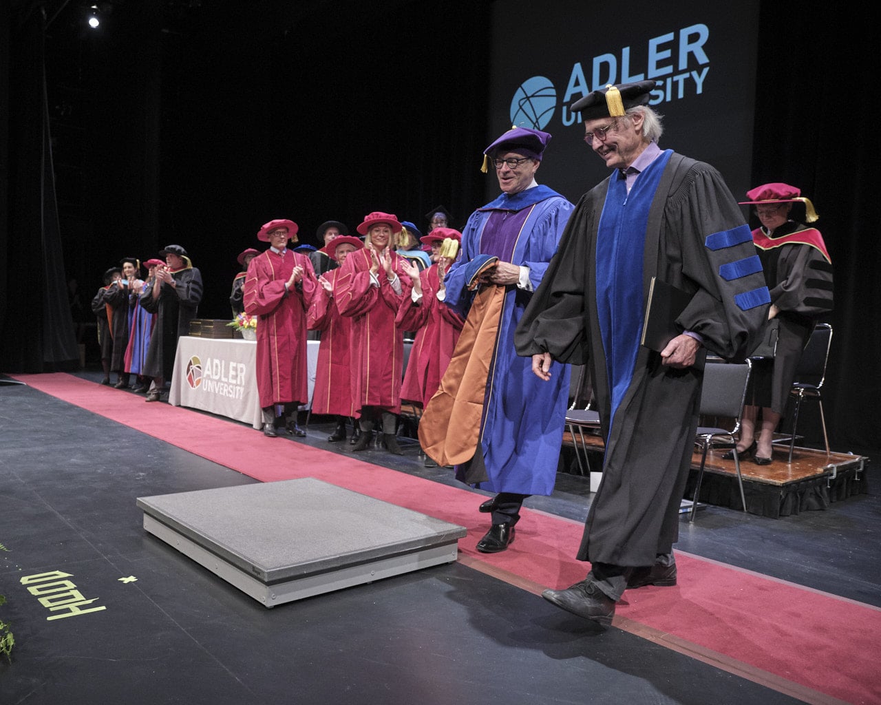 Two men walk of stage at a university commencement ceremony