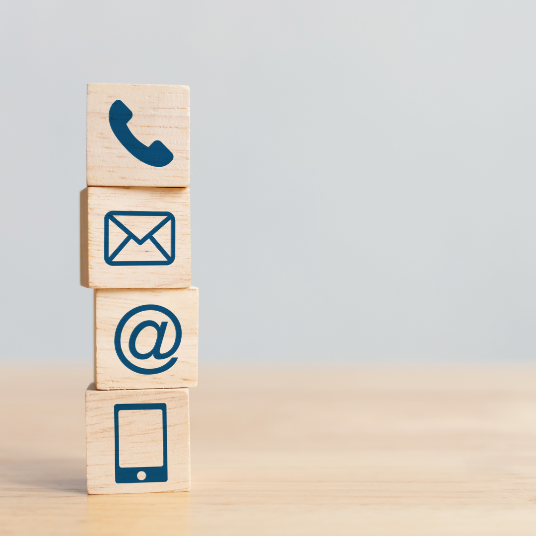 Stack of four wooden blocks with blue contact icons: phone, envelope, at symbol, and smartphone on a light background.