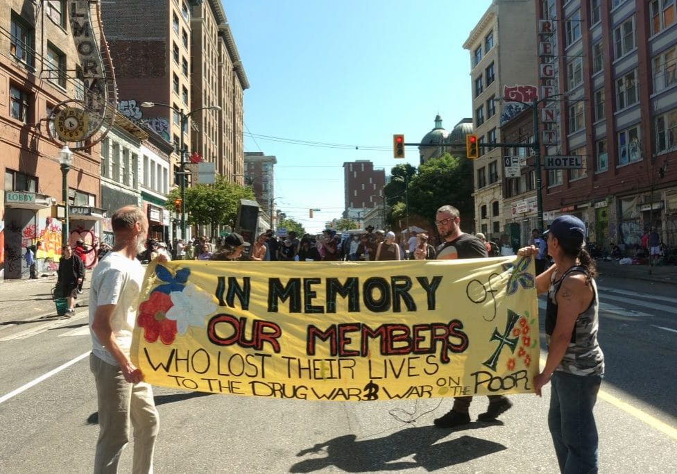 Two people carry a large banner down the street that reads "In Memory Our Members"